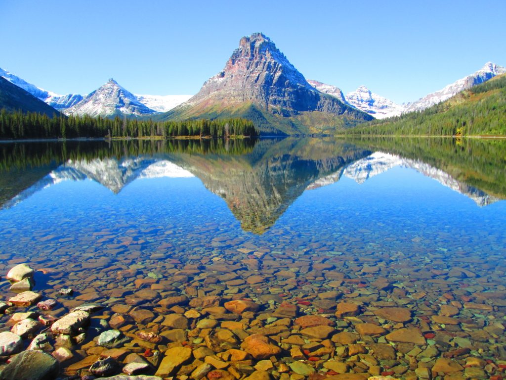 Dead-calm water on a lake in Glacier National Park, with a reflection of the Rockies silhoutted within it. 
